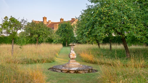 Sundial surrounded by long grassed and trees, with Lytes Cary Manor in the background